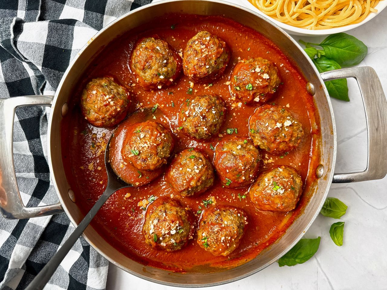 meatballs and marinara sauce in a pan with a black serving spoon