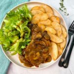 Pork Chops with Mushroom Gravy on a white plate with potato wedges and a green salad
