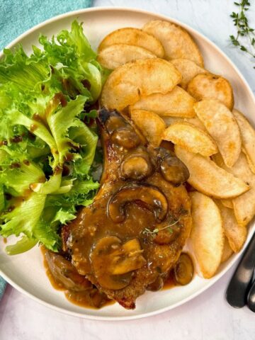 Pork Chops with Mushroom Gravy on a white plate with potato wedges and a green salad