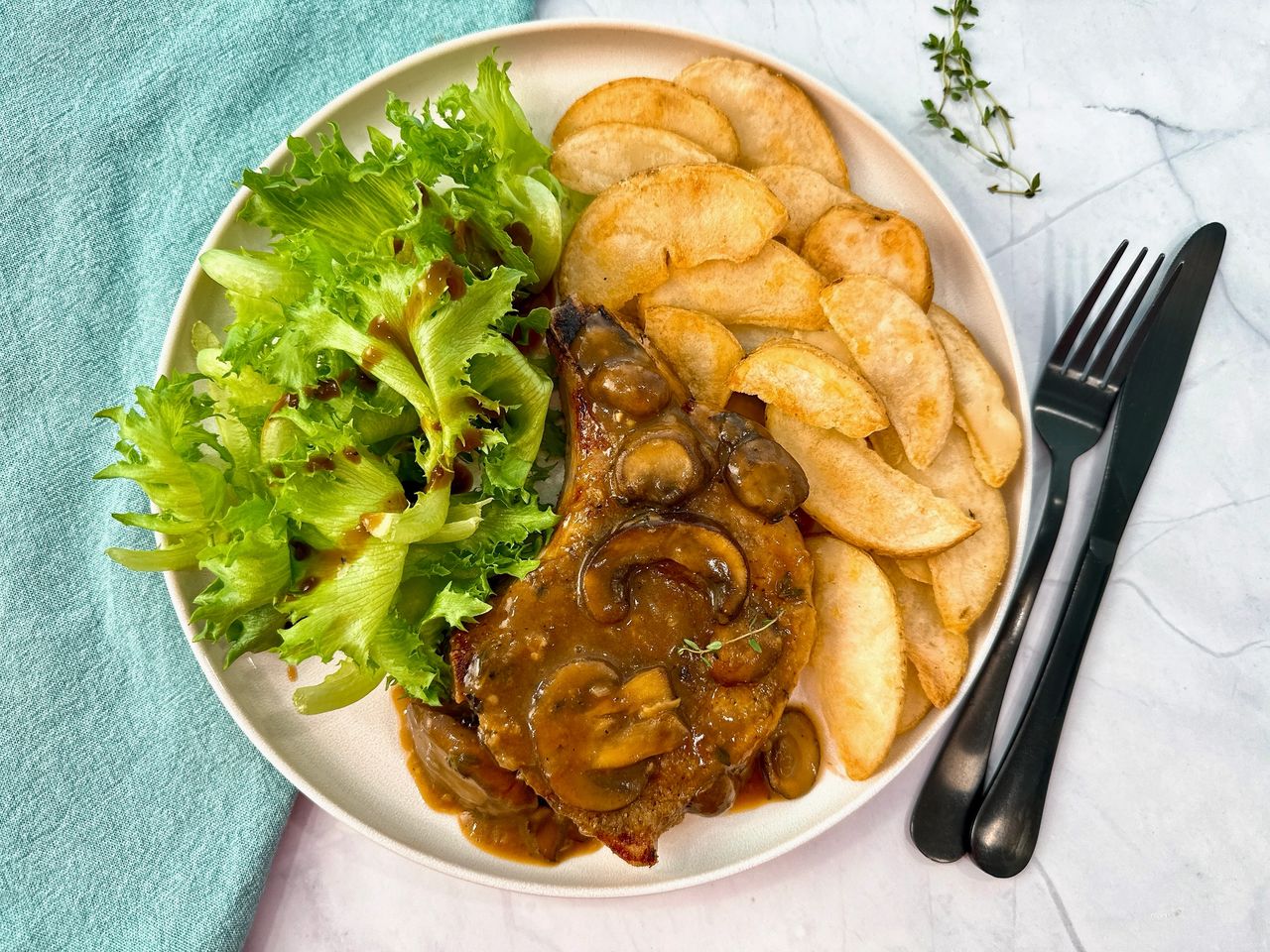 Pork Chops with Mushroom Gravy on a white plate with potato wedges and a green salad