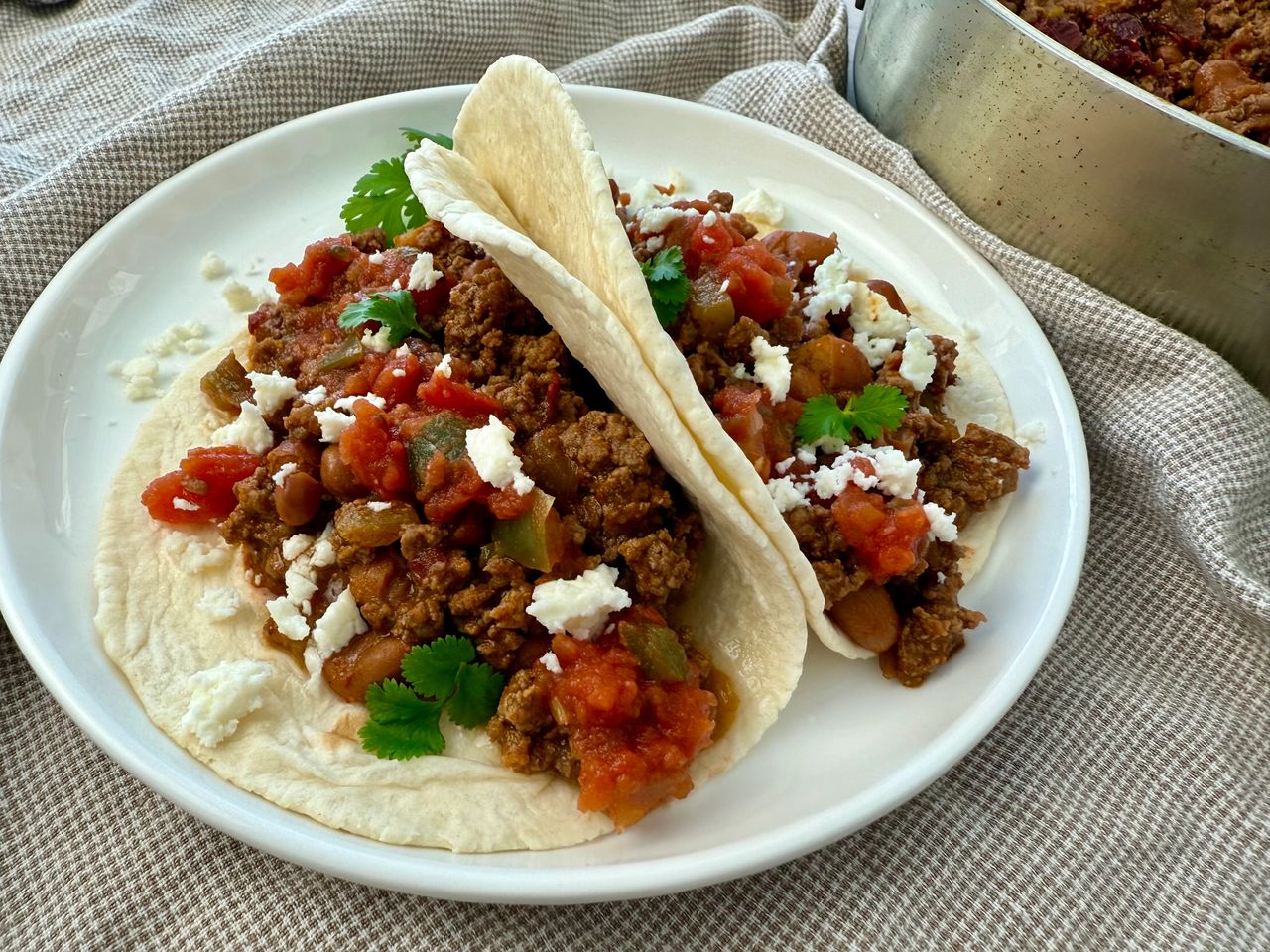 ground beef and bean soft tacos on a white plate with crumbled cheese garnish