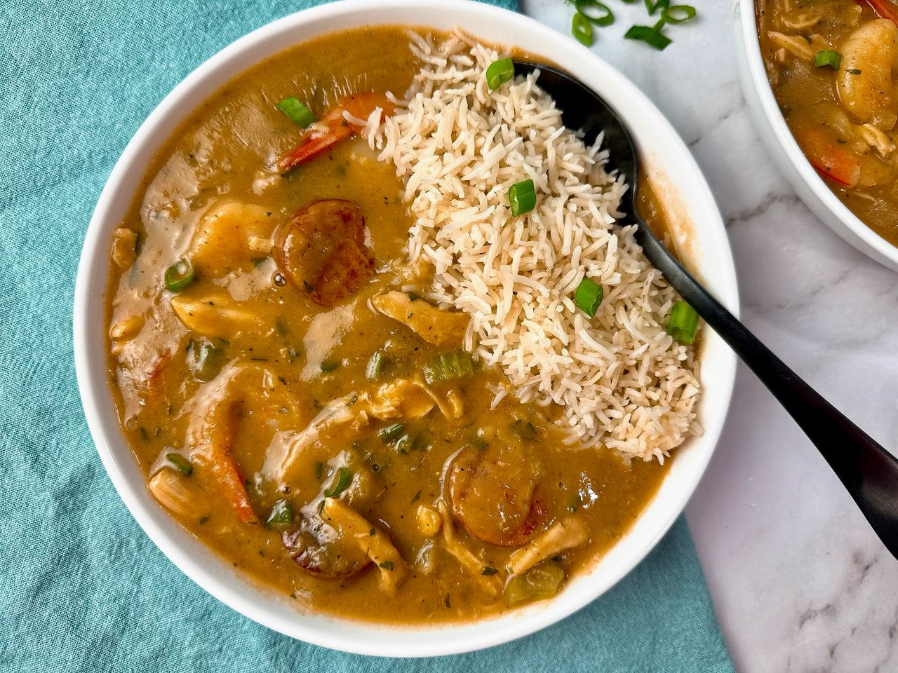 Cajun gumbo and rice in a white bowl with a black spoon