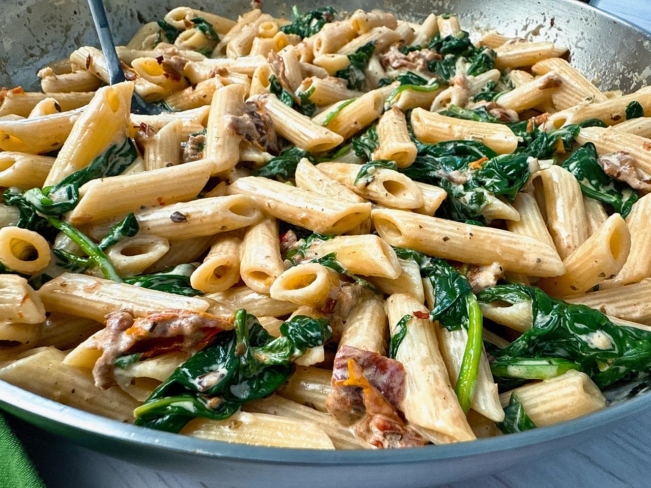 penne pasta, spinach, and sun dried tomatoes in a skillet 