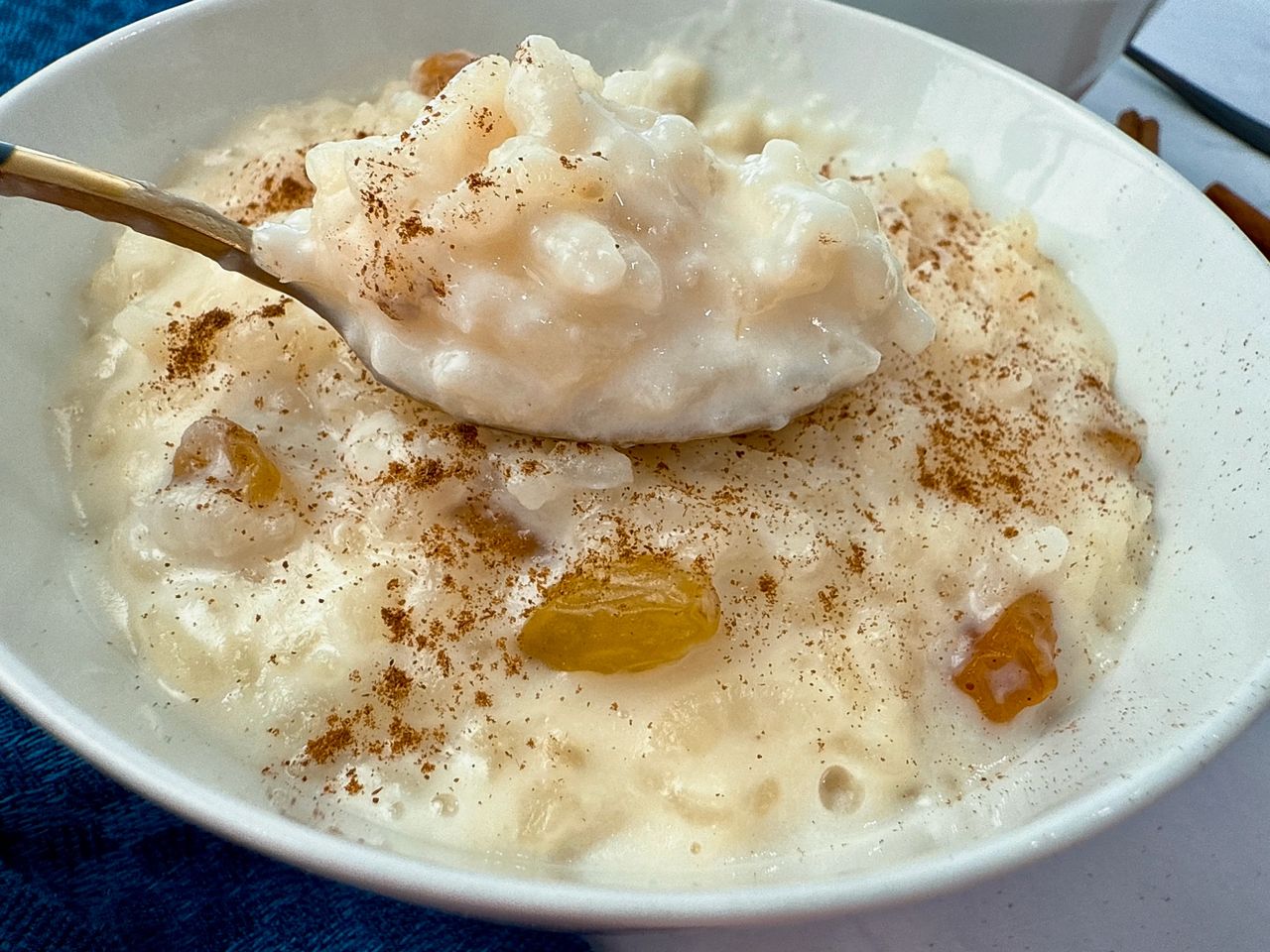 rice pudding in a white bowl with a black spoon and cinnamon sticks on the side