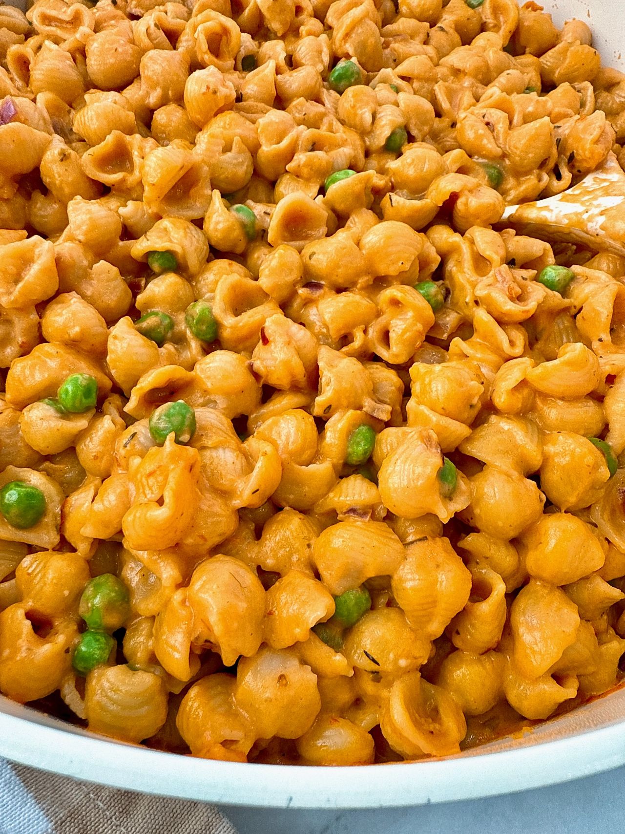 Creamy Pasta and Peas in a white saucepan with a white spoon and cheese on the side