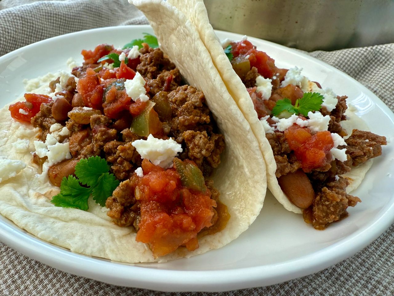 Beef and Bean Street Tacos ground beef and bean soft tacos on a white plate with crumbled cheese garnish