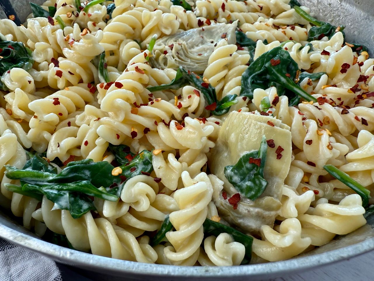 pasta with spinach and artichoke hearts in a skillet
