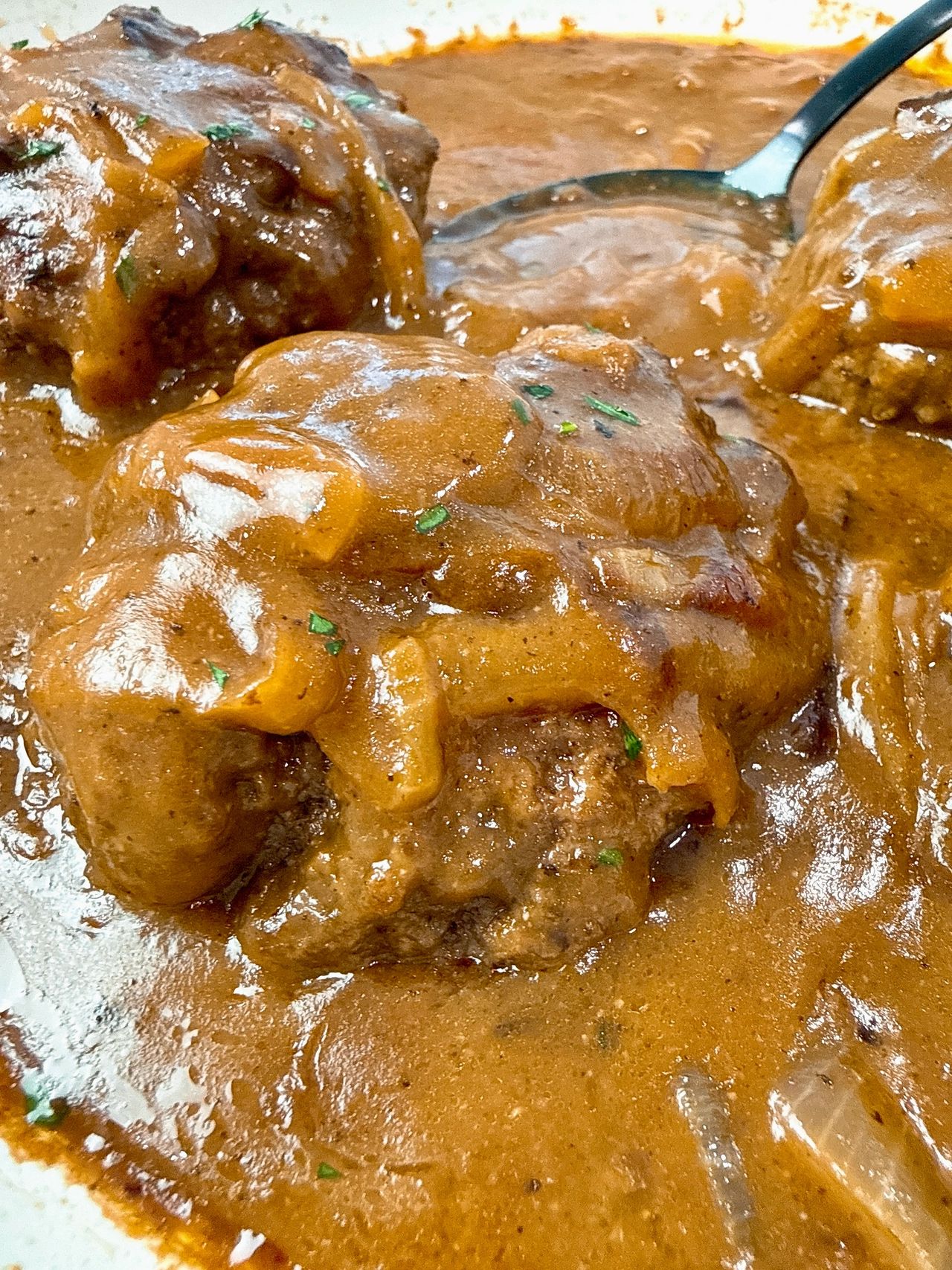 hamburger steaks and gravy with a black serving spoon