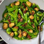 brussels sprouts, snow peas, and sun dried tomatoes in a white skillet