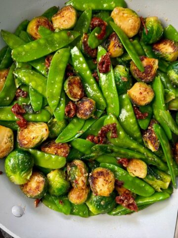 brussels sprouts, snow peas, and sun dried tomatoes in a white skillet