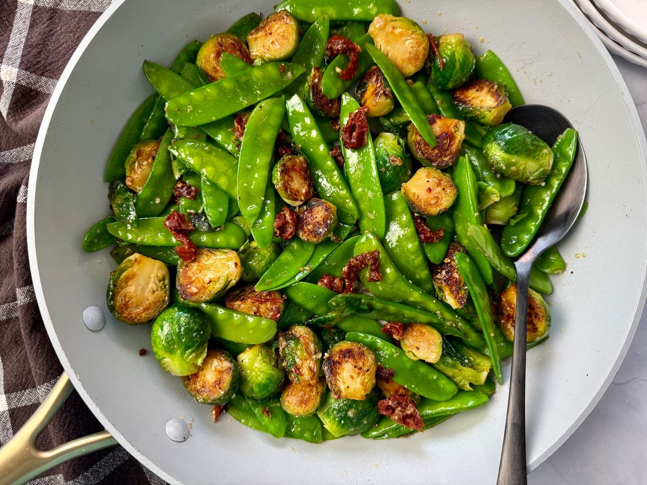brussels sprouts, snow peas, and sun dried tomatoes in a white skillet