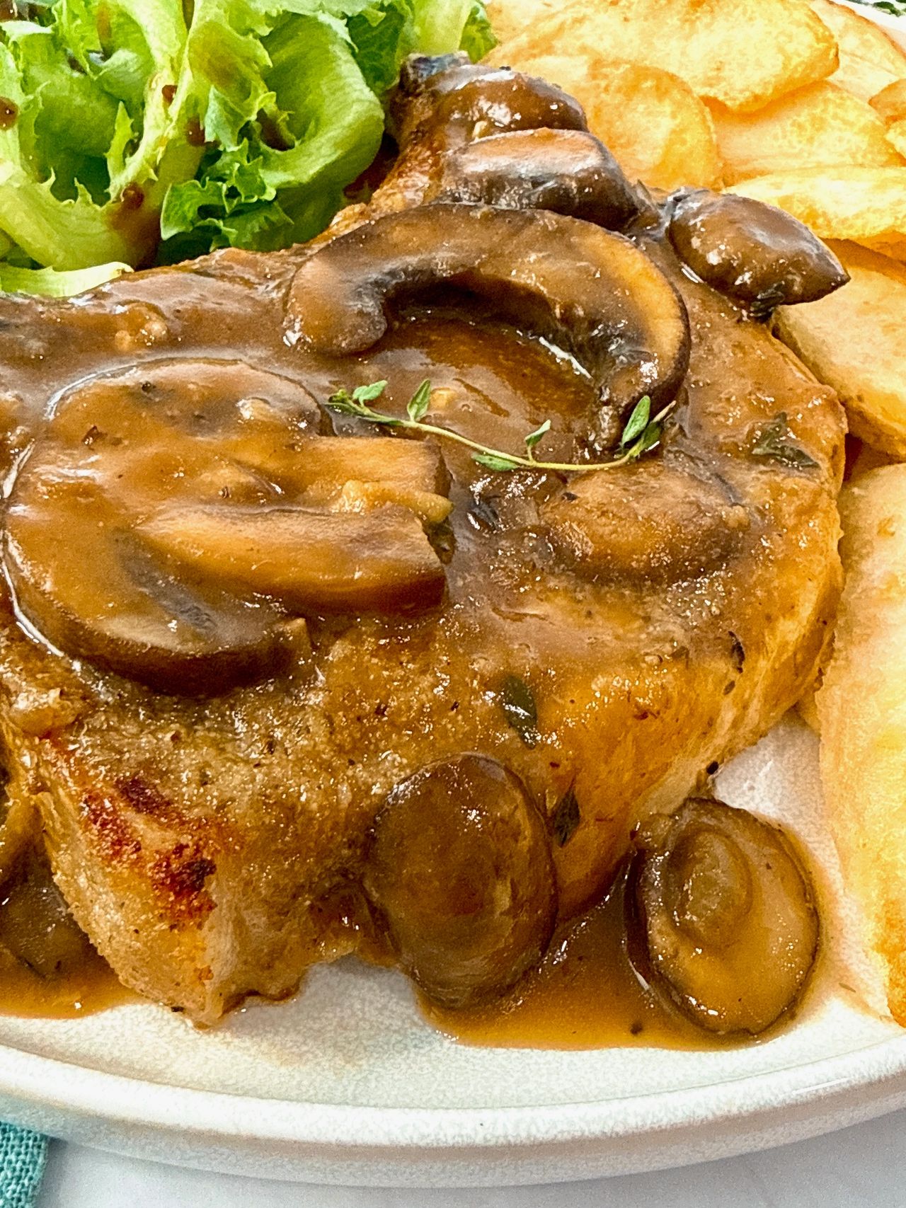 Pork Chops with Mushroom Gravy on a white plate with potato wedges and a green salad