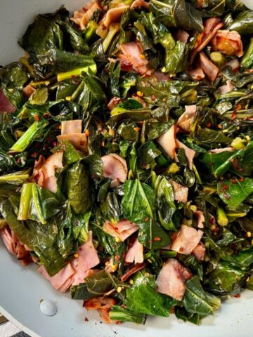 collard greens and ham in a white skillet
