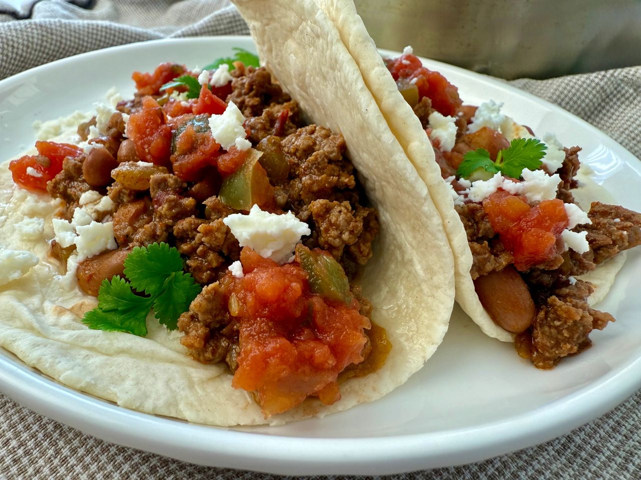 ground beef and bean soft tacos on a white plate with crumbled cheese garnish