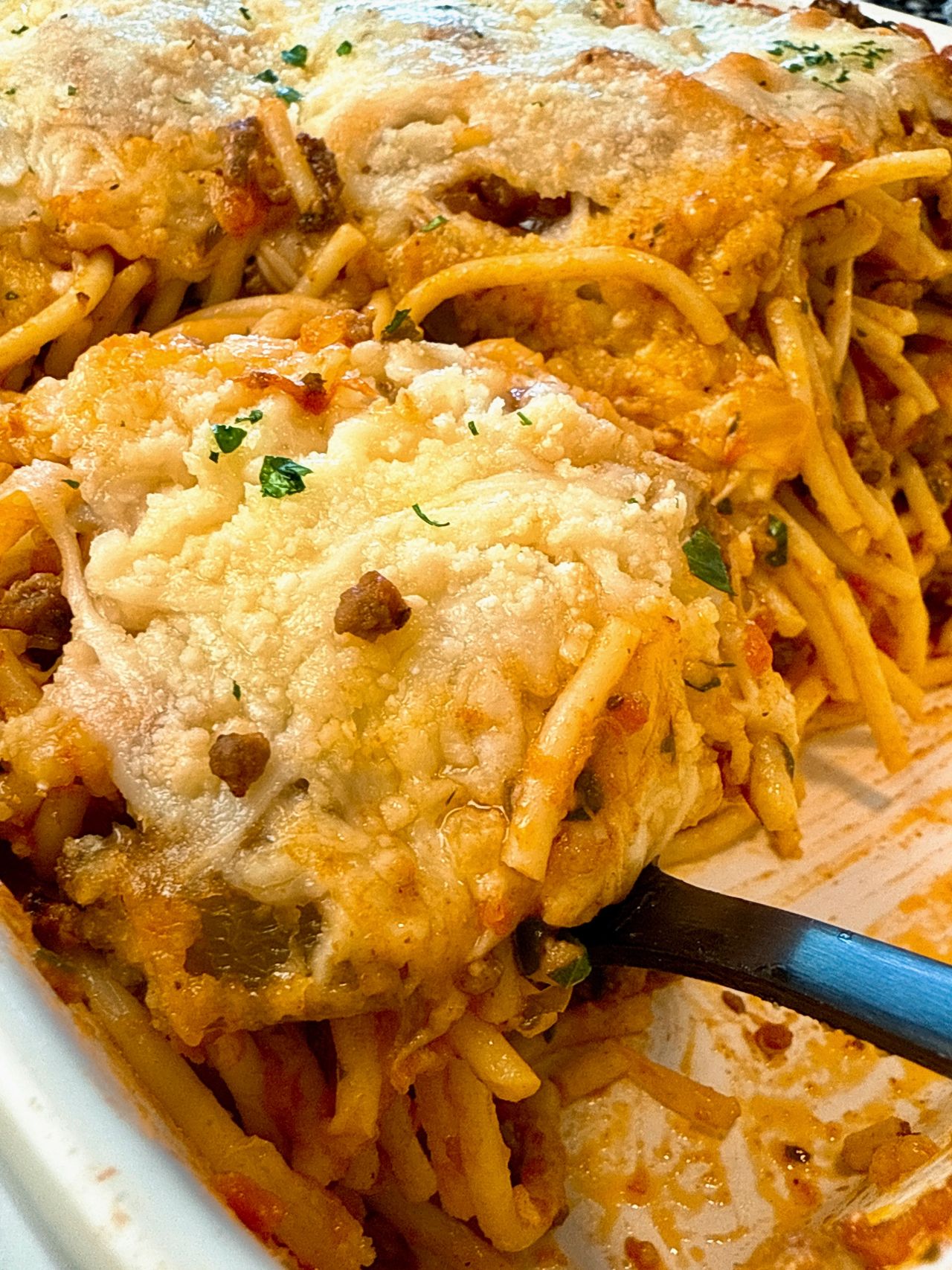 baked spaghetti in a baking dish with a black spoon