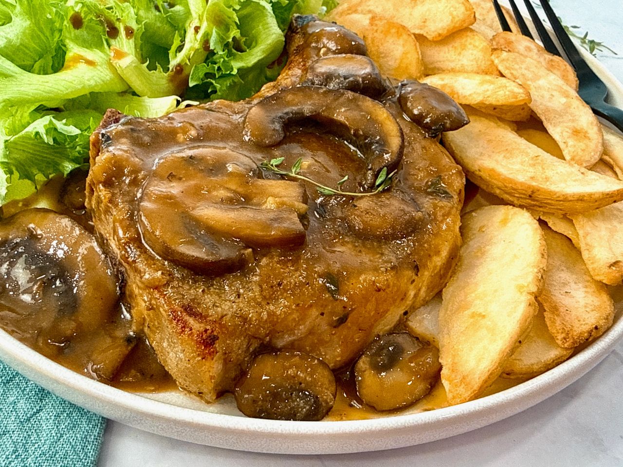 Pork Chops with Mushroom Gravy on a white plate with potato wedges and a green salad