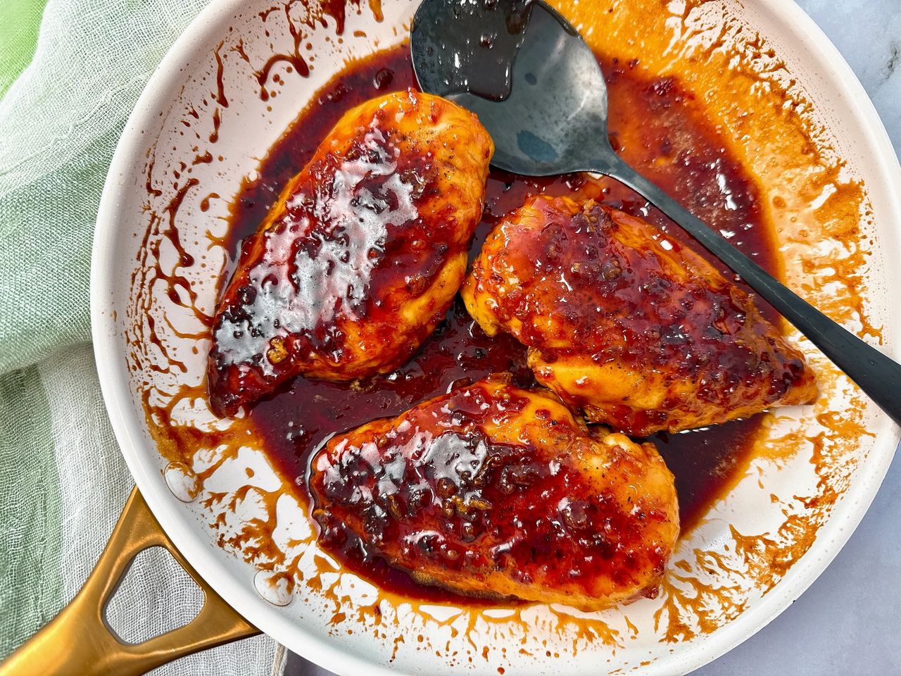 hot honey chicken in a white skillet with a black spoon