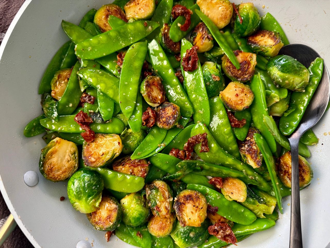 brussels sprouts, snow peas, and sun dried tomatoes in a white skillet