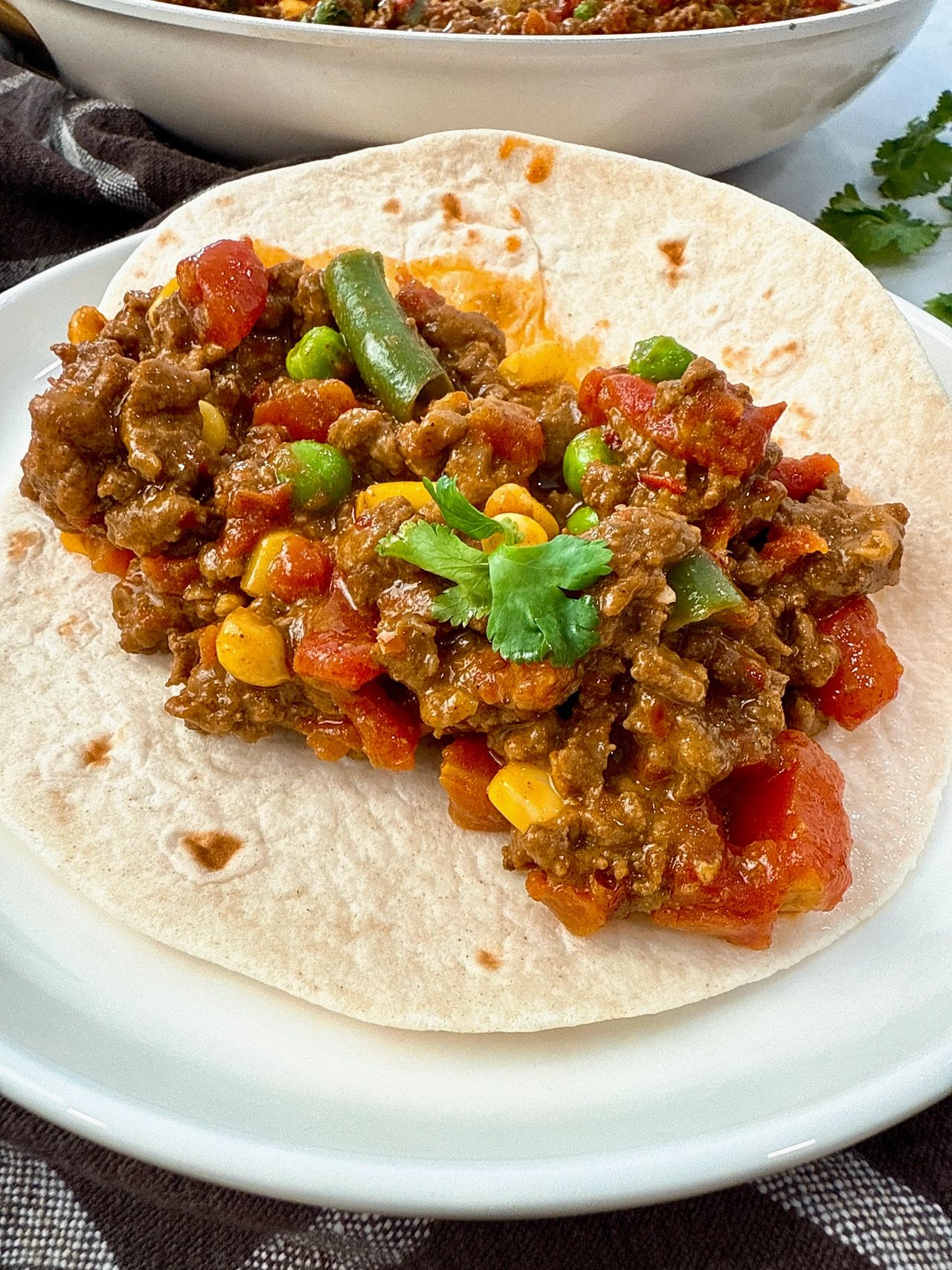 ground beef and vegetables in a tortilla on a white plate