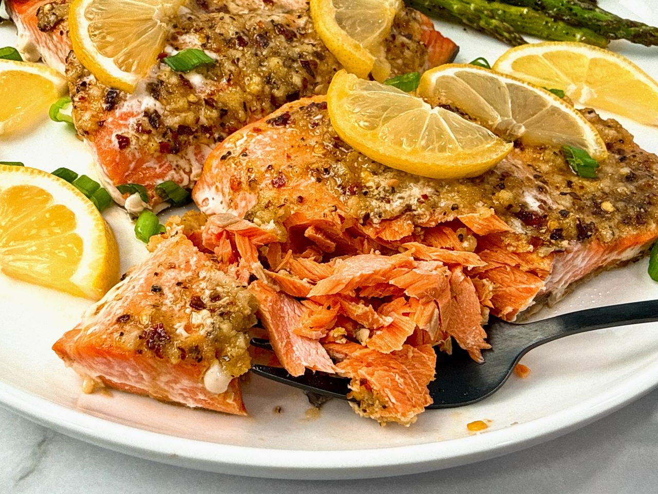 salmon on a white plate with lemon slices and a black fork