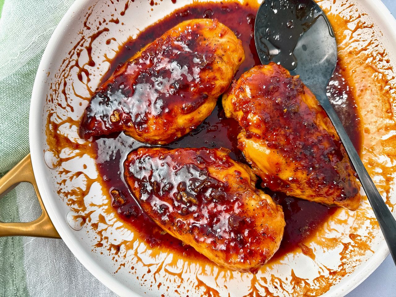 hot honey chicken in a white skillet with a black spoon