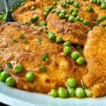 parmesan chicken and peas in wine sauce in white skillet