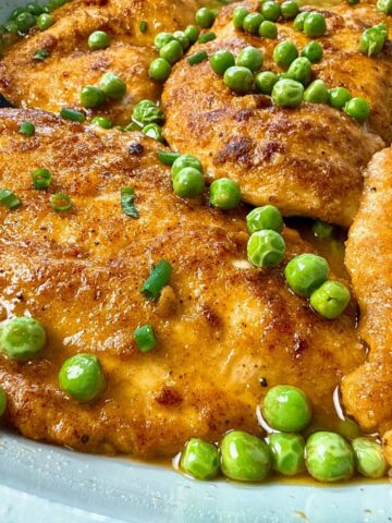 parmesan chicken and peas in wine sauce in white skillet