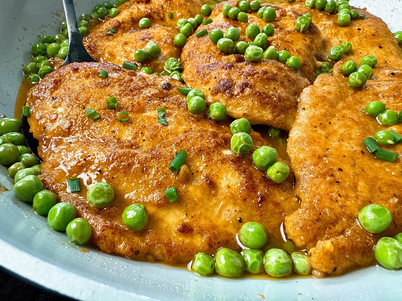 parmesan chicken and peas in wine sauce in white skillet