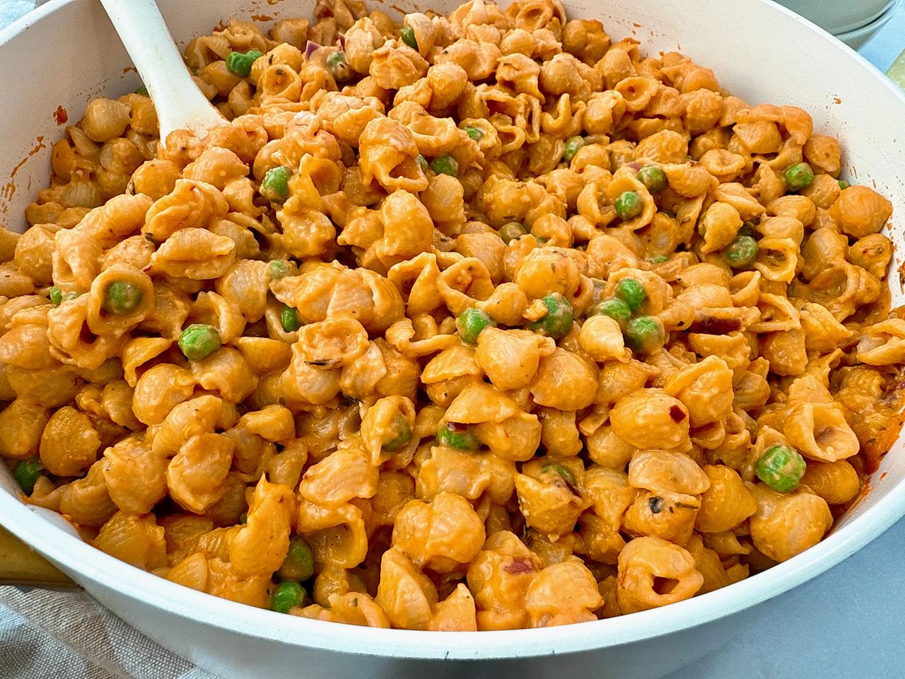 Creamy Pasta and Peas in a white saucepan with a white spoon and cheese on the side