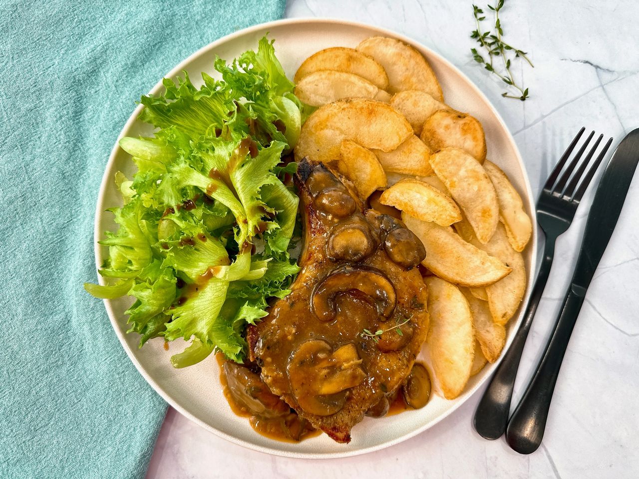 Pork Chops with Mushroom Gravy on a white plate with potato wedges and a green salad