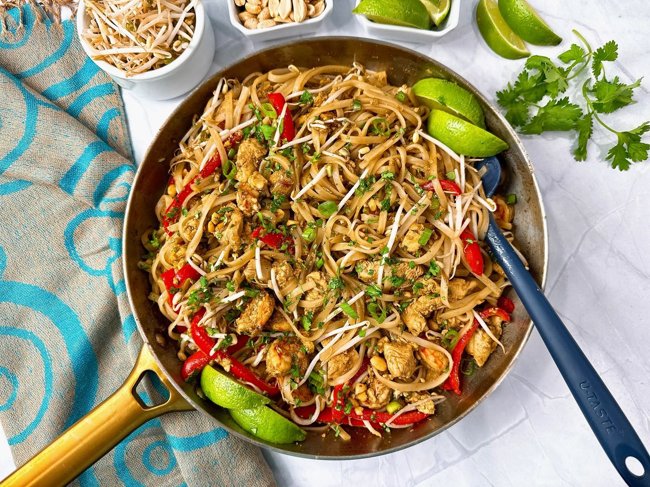 pad thai in a silver skillet with peanuts on the side