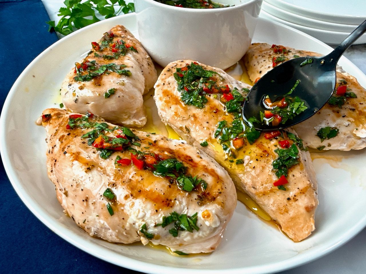 grilled chicken and bowl of chimichurri sauce on a white plate with a black spoon