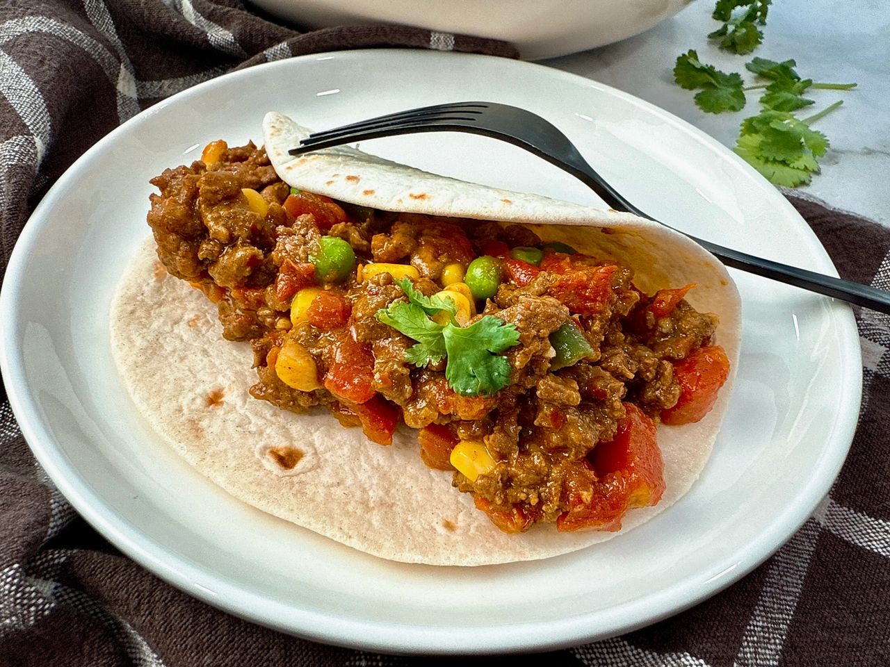 ground beef and vegetables in a tortilla on a white plate