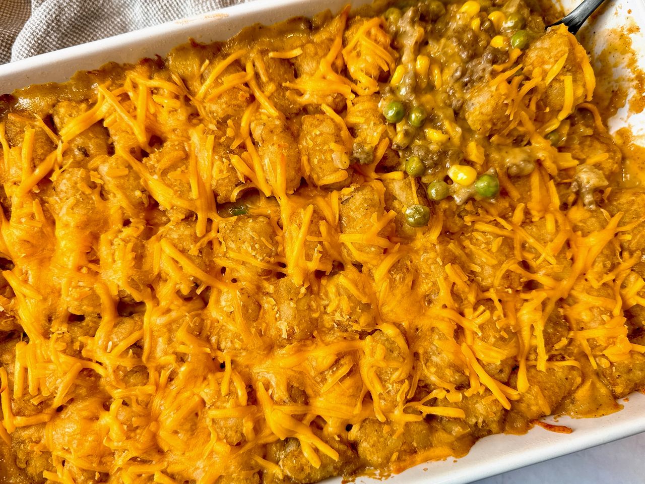 tater tot casserole in a white baking dish and on a spoon
