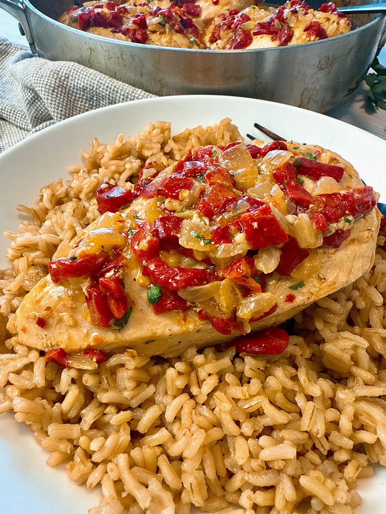 chicken breast with roasted red peppers over rice on a white plate