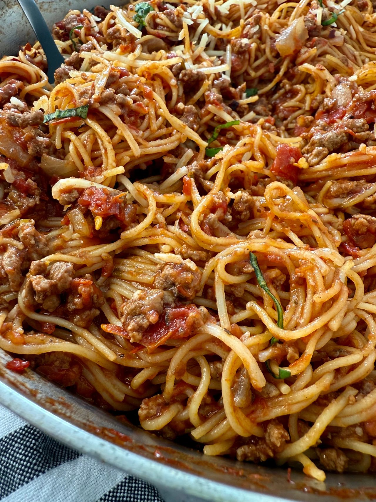 pasta bolognese in a silver pan with a black spoon