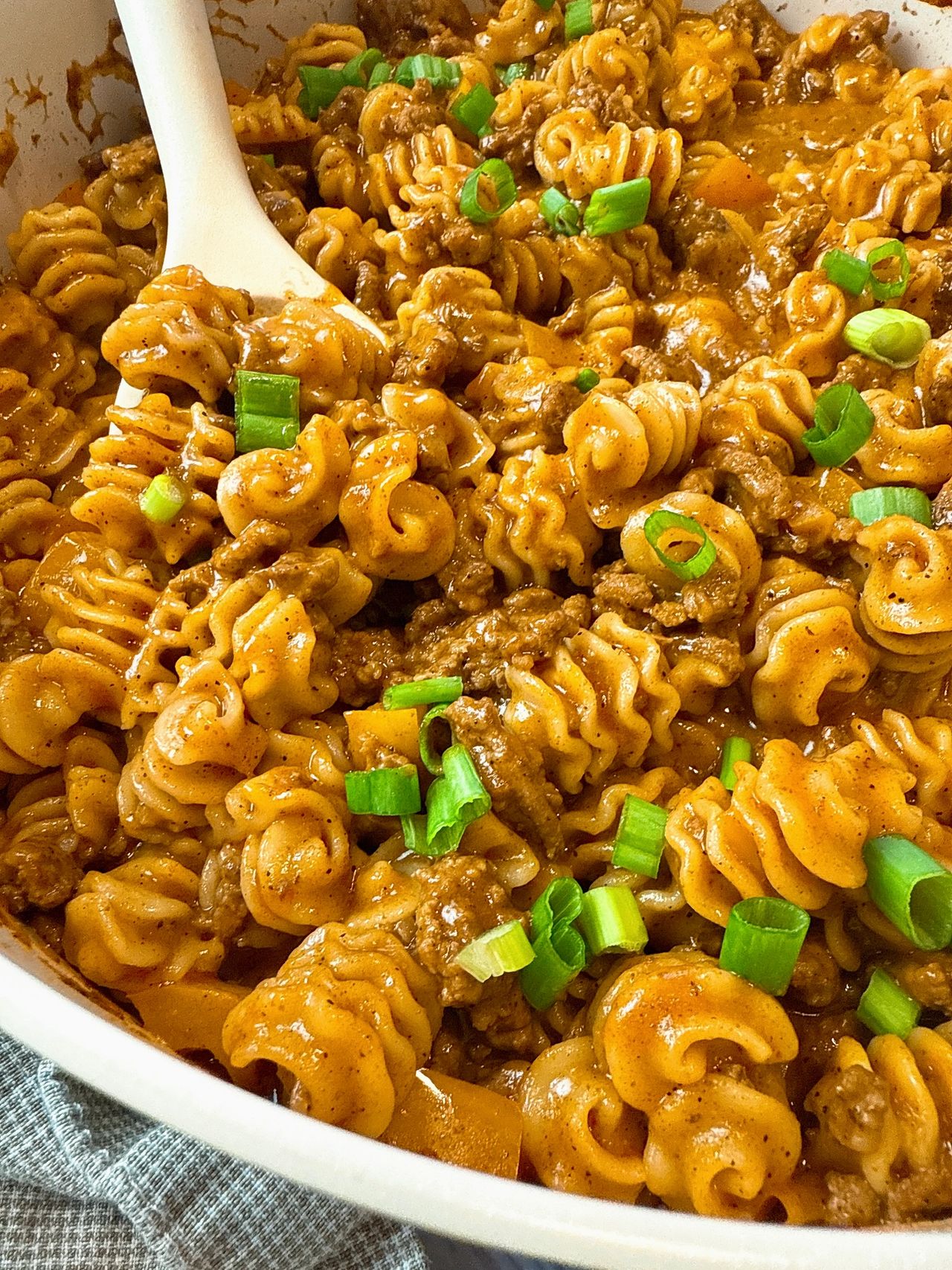 beef and pasta in an enchilada sauce in a white pan with a white spoon