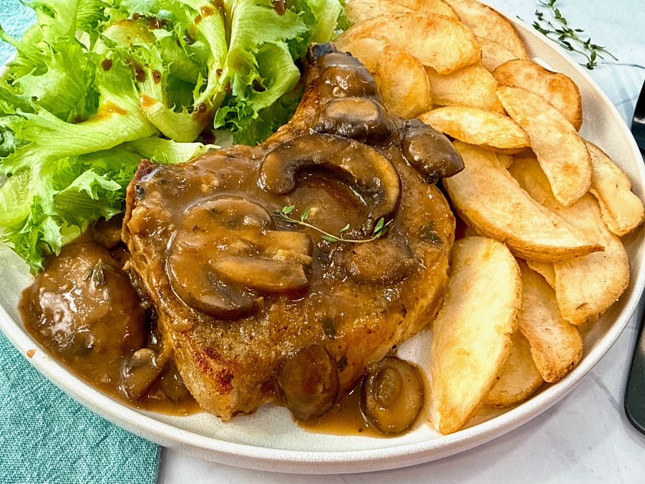 Pork Chops with Mushroom Gravy on a white plate with potato wedges and a green salad