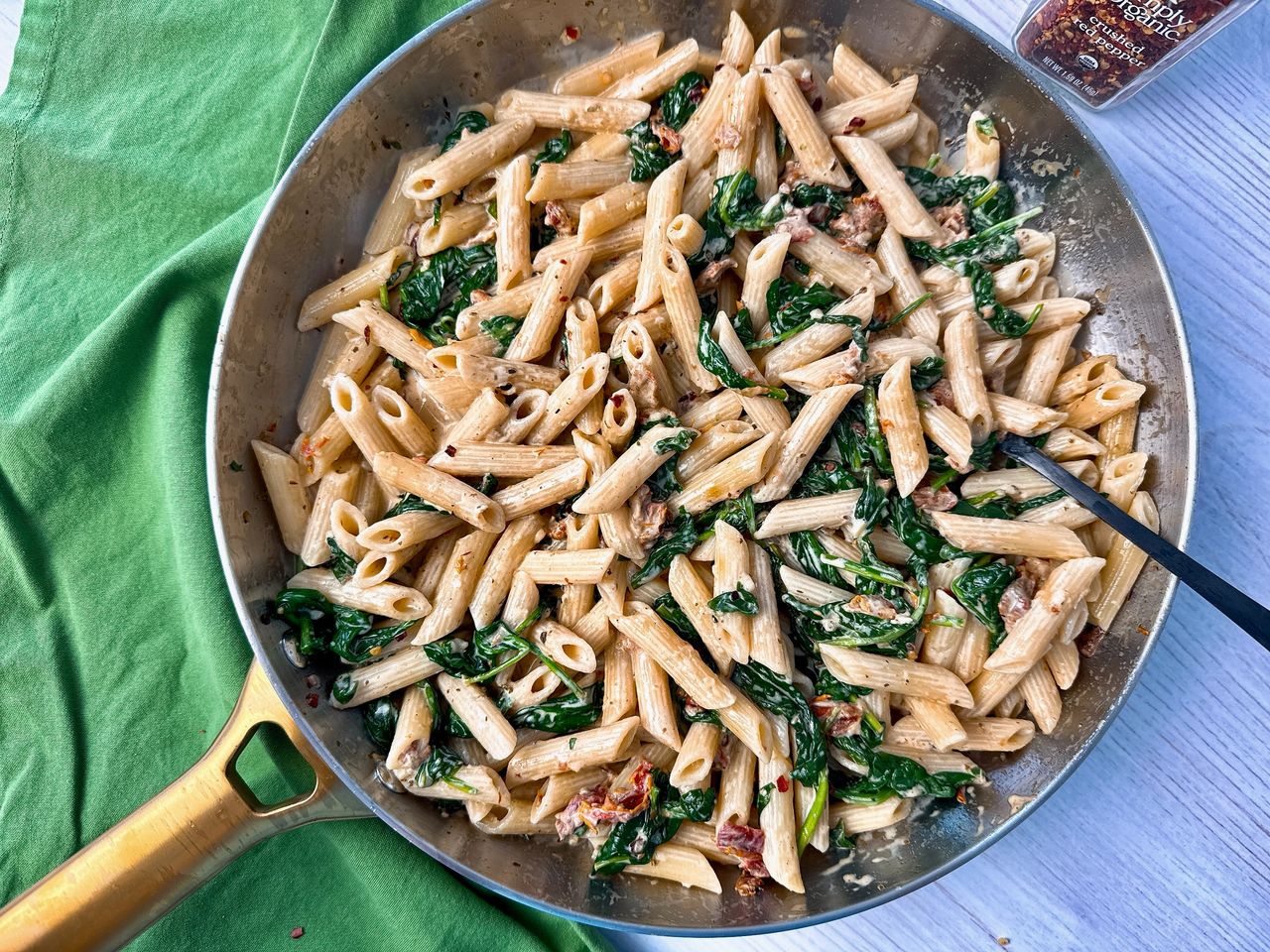 penne pasta, spinach, and sun dried tomatoes in a skillet 