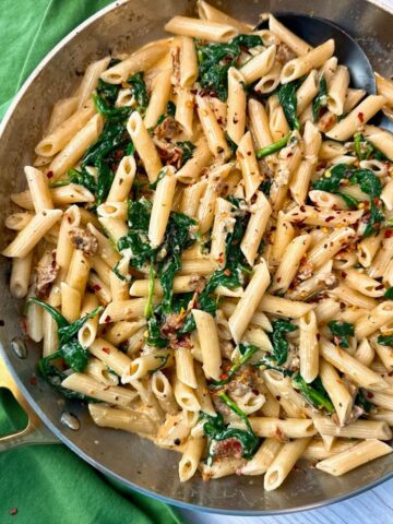 penne pasta, spinach, and sun dried tomatoes in a skillet