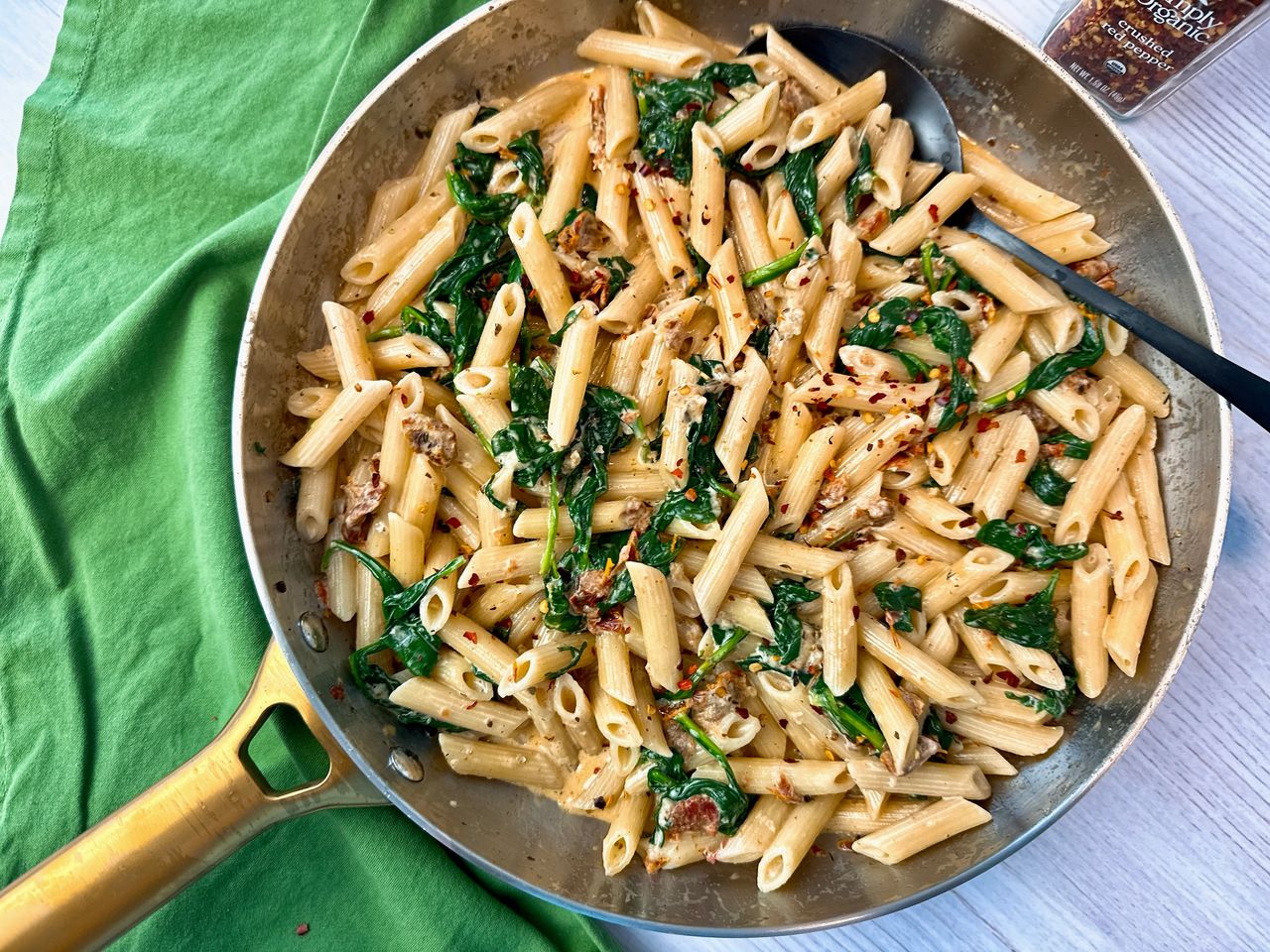 penne pasta, spinach, and sun dried tomatoes in a skillet 