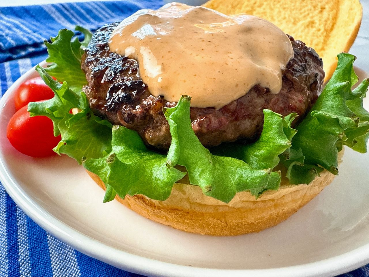 burger on a bun with lettuce and spicy sauce