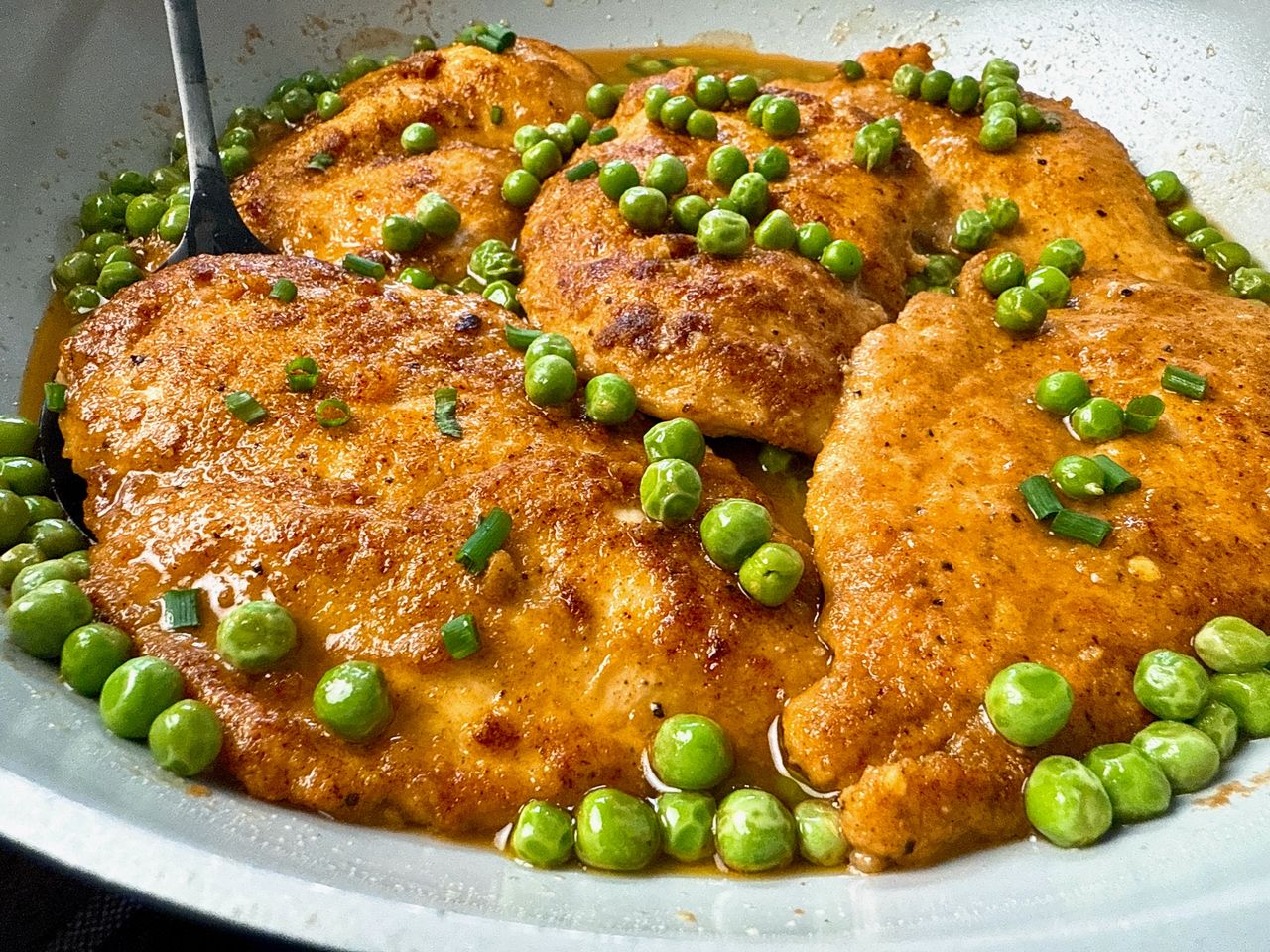 parmesan chicken and peas in wine sauce in white skillet