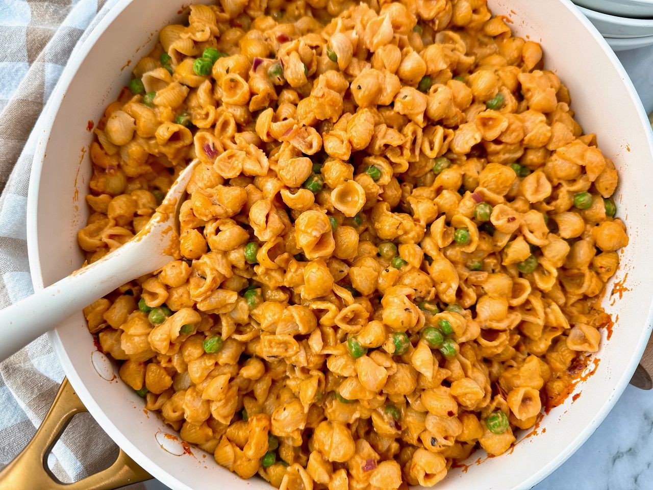 Creamy Pasta and Peas in a white saucepan with a white spoon and cheese on the side