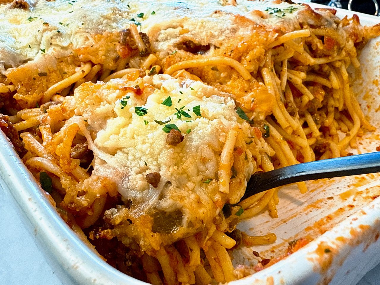 baked spaghetti in a baking dish with a black spoon
