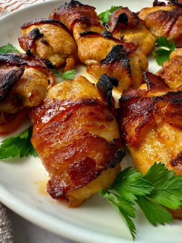 bacon wrapped chicken on a white plate with parsley garnish