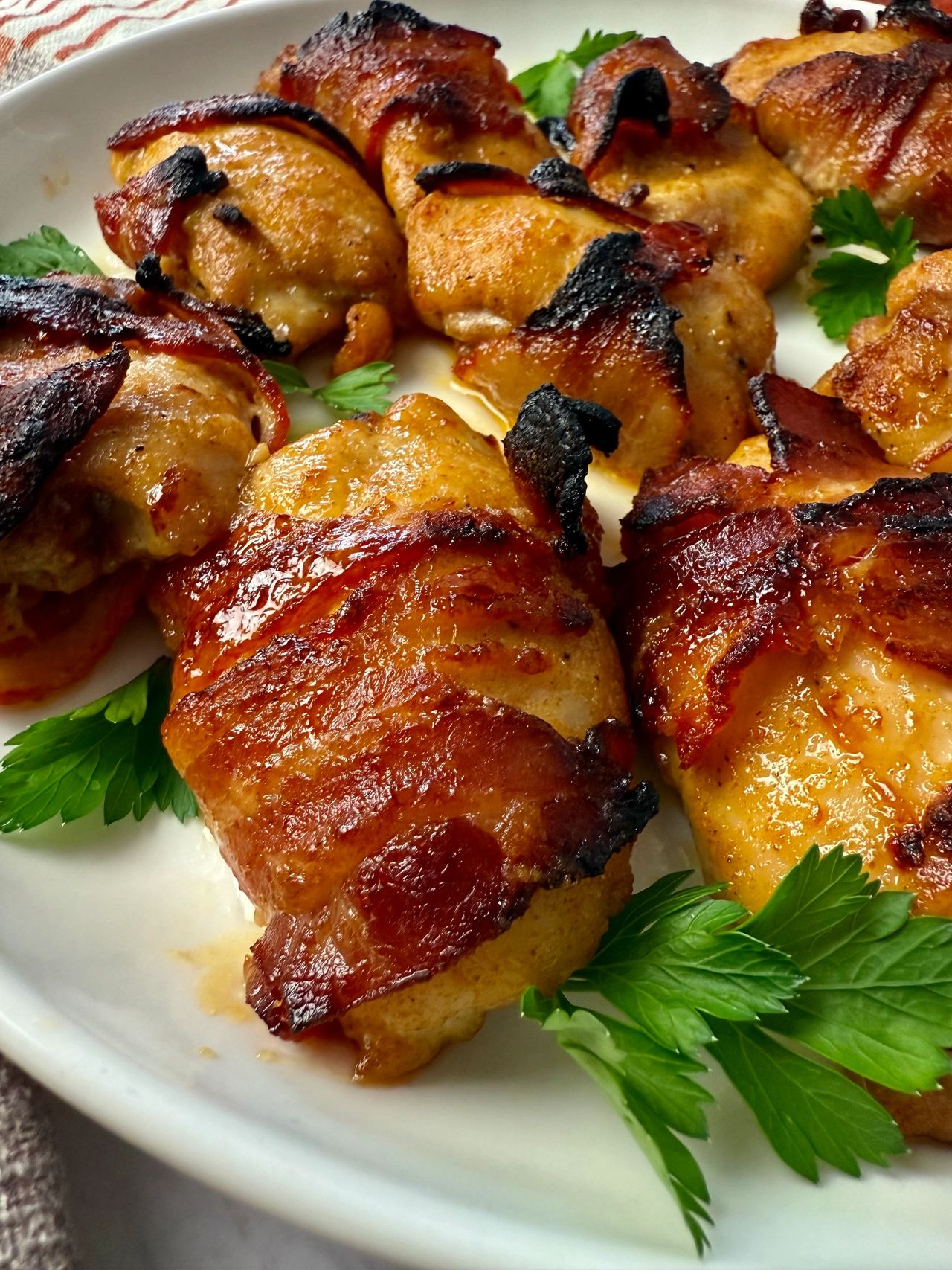 bacon wrapped chicken on a white plate with parsley garnish