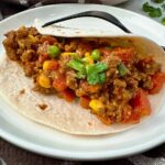 ground beef and vegetables in a tortilla on a white plate