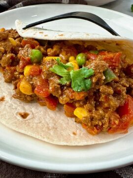 ground beef and vegetables in a tortilla on a white plate