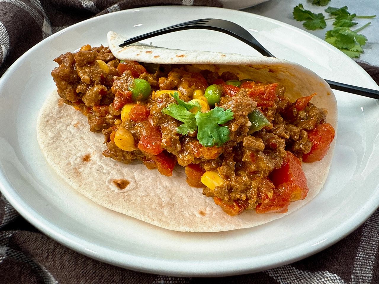 ground beef and vegetables in a tortilla on a white plate